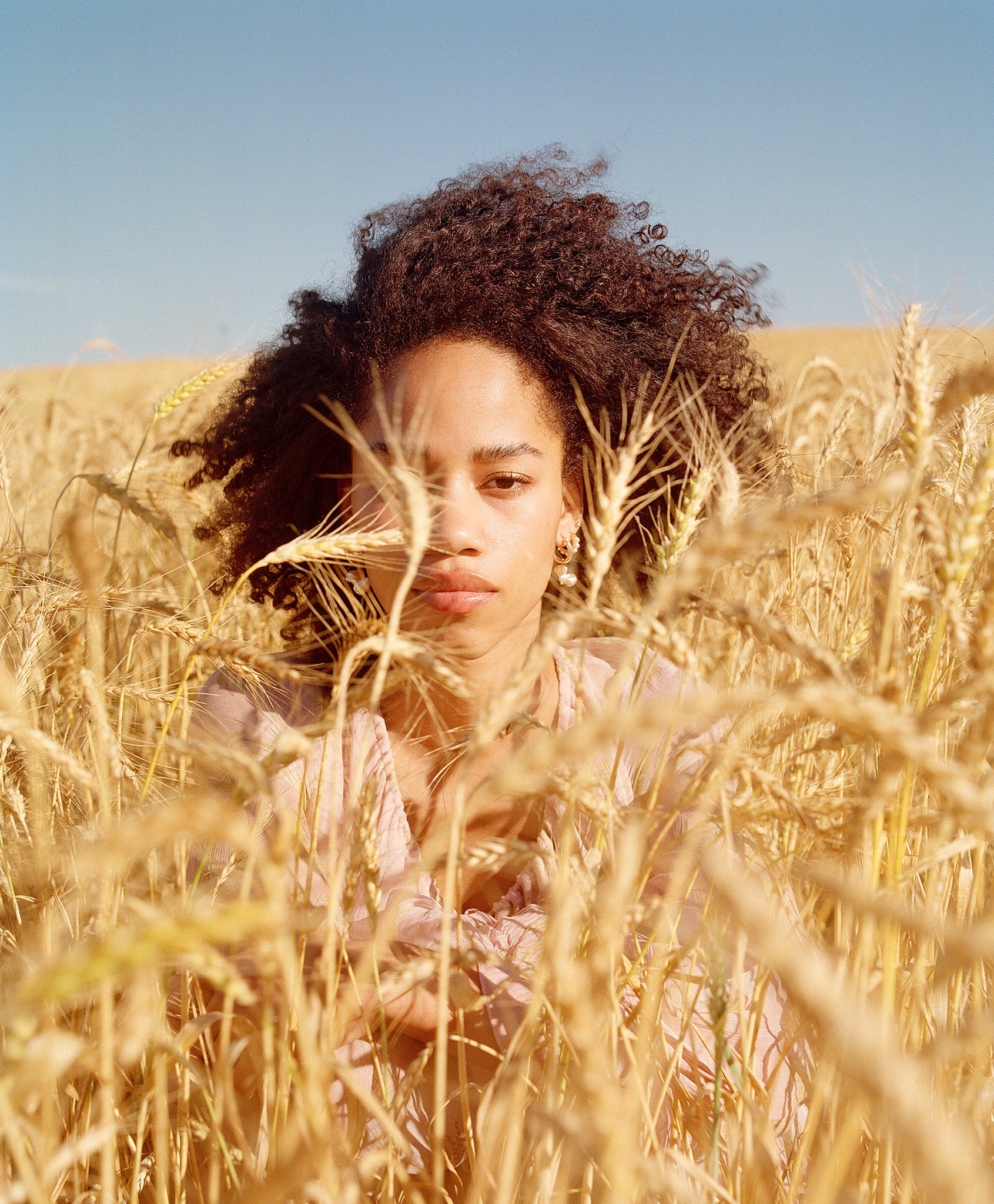 A model with an Afro surrounded by a wheat field is styled with Curly Angels Hallelujah Curl Activator - vegan, cruelty-free hair care