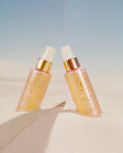 curly angels sacred scent fragrance  mist set in white sand resting against a mirror with blue sky  vegan haircare, cruelty-free, suitable for all curl types